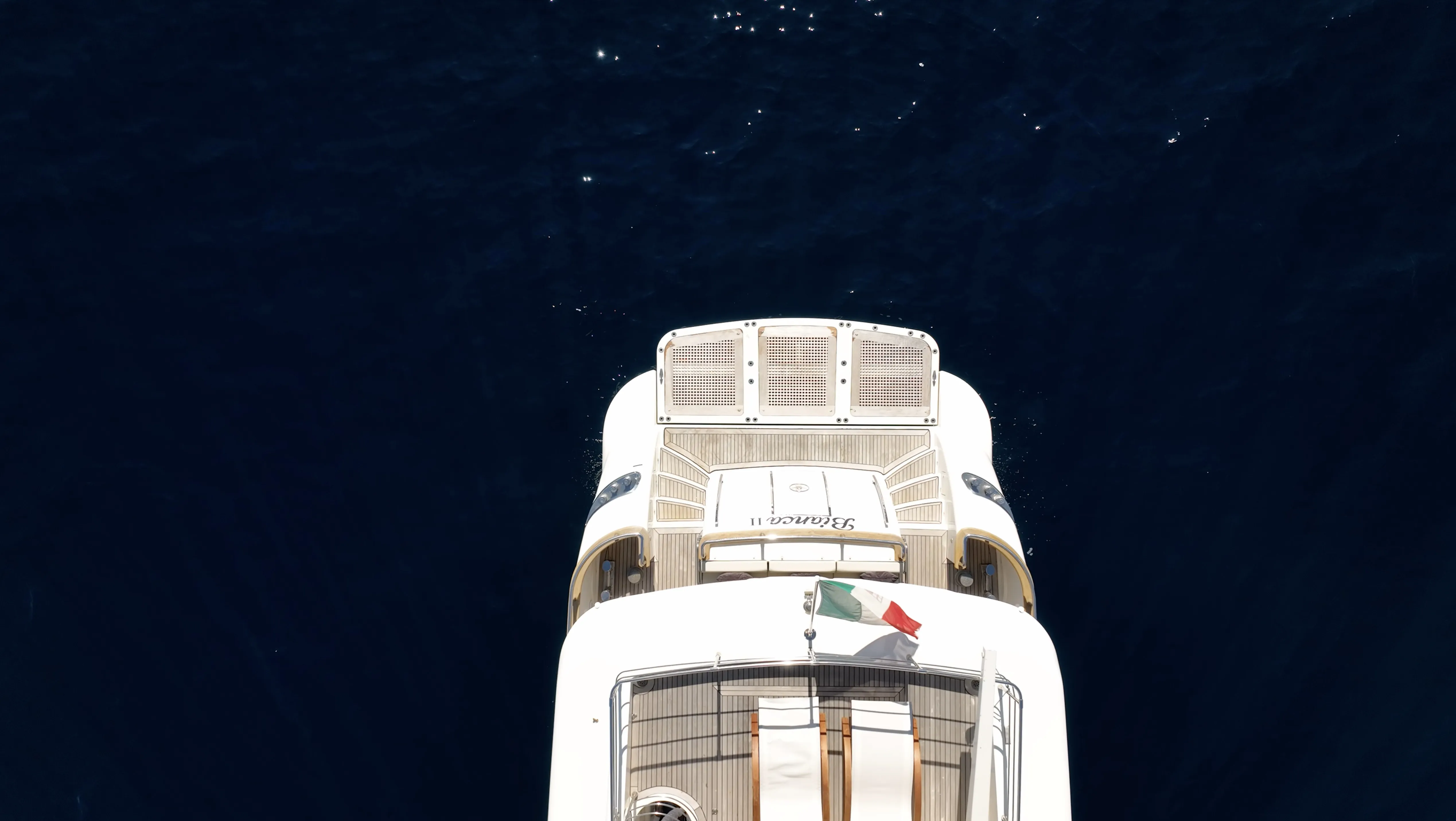 Bianca II seen from directly above, stern and Italian flag against deep blue water
