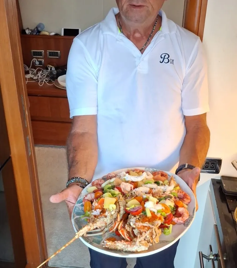 The captain carrying a platter of lobster and prawns out of the galley, in a Bianca II polo shirt