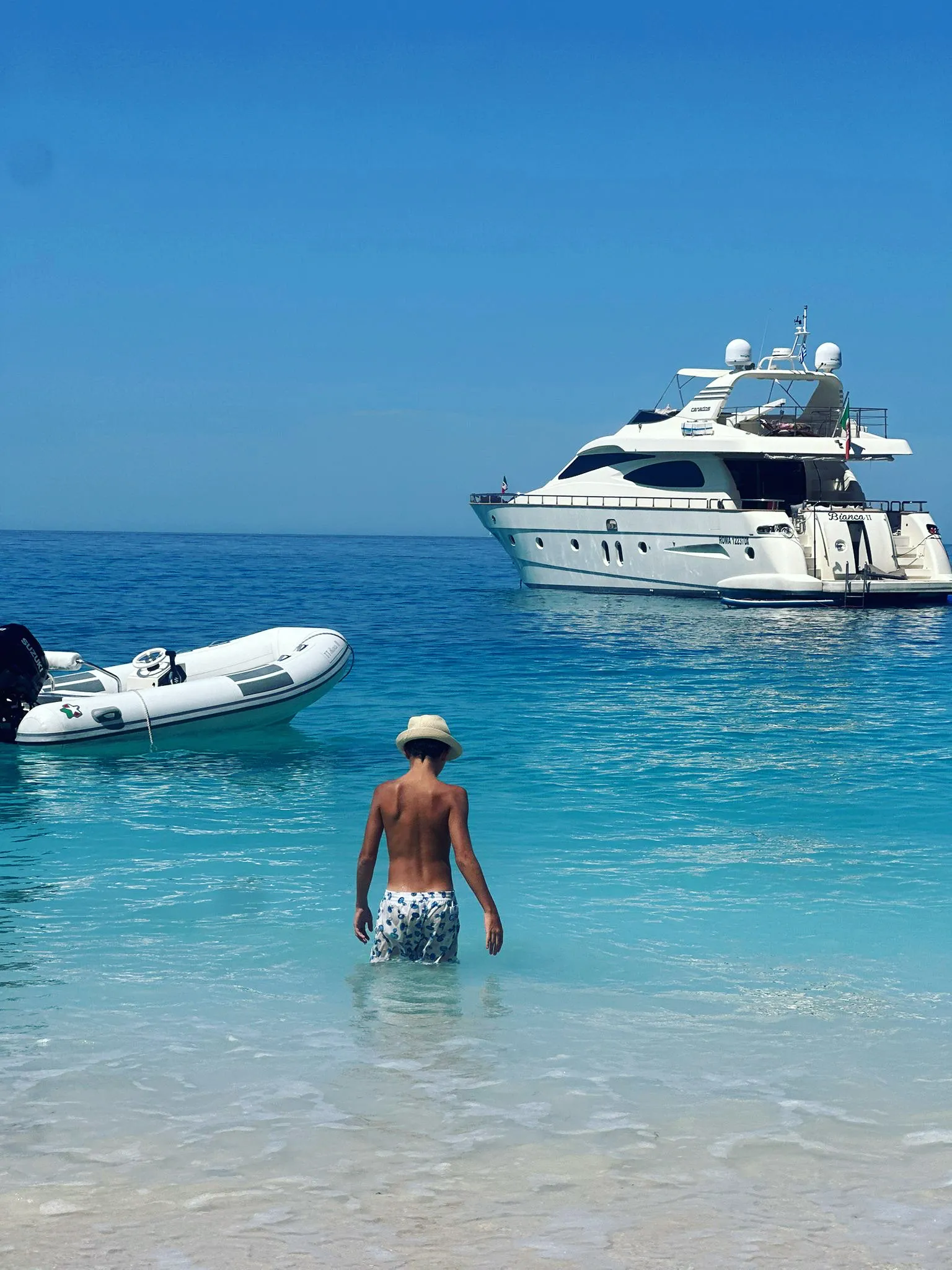 The tender pulled up on a pale sand beach, Bianca II at anchor beyond