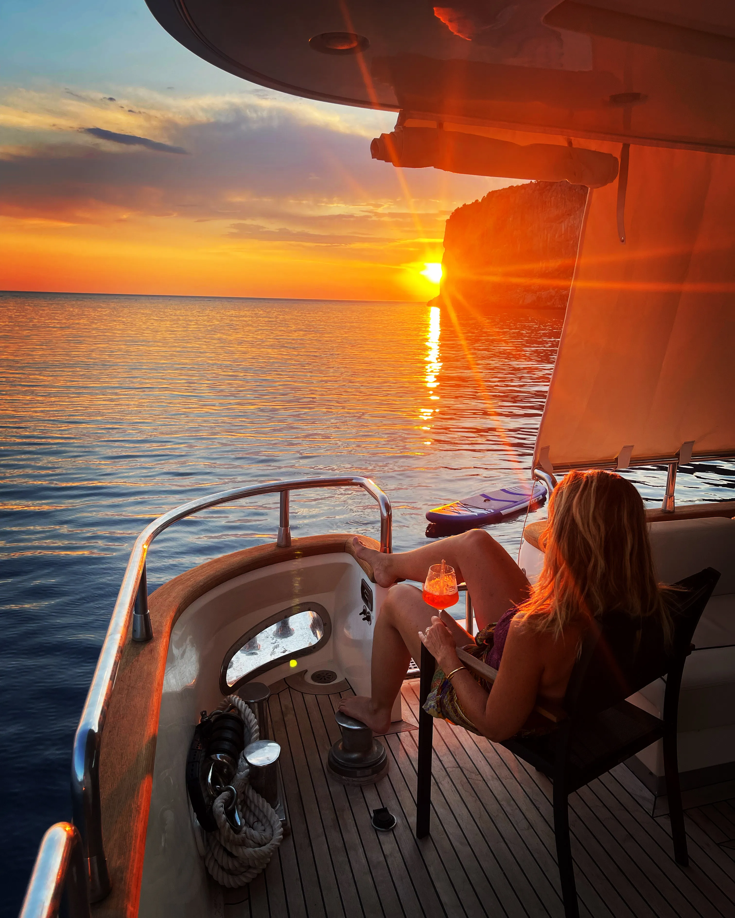 The sun going down behind the headland seen from the aft deck, a paddleboard in the water