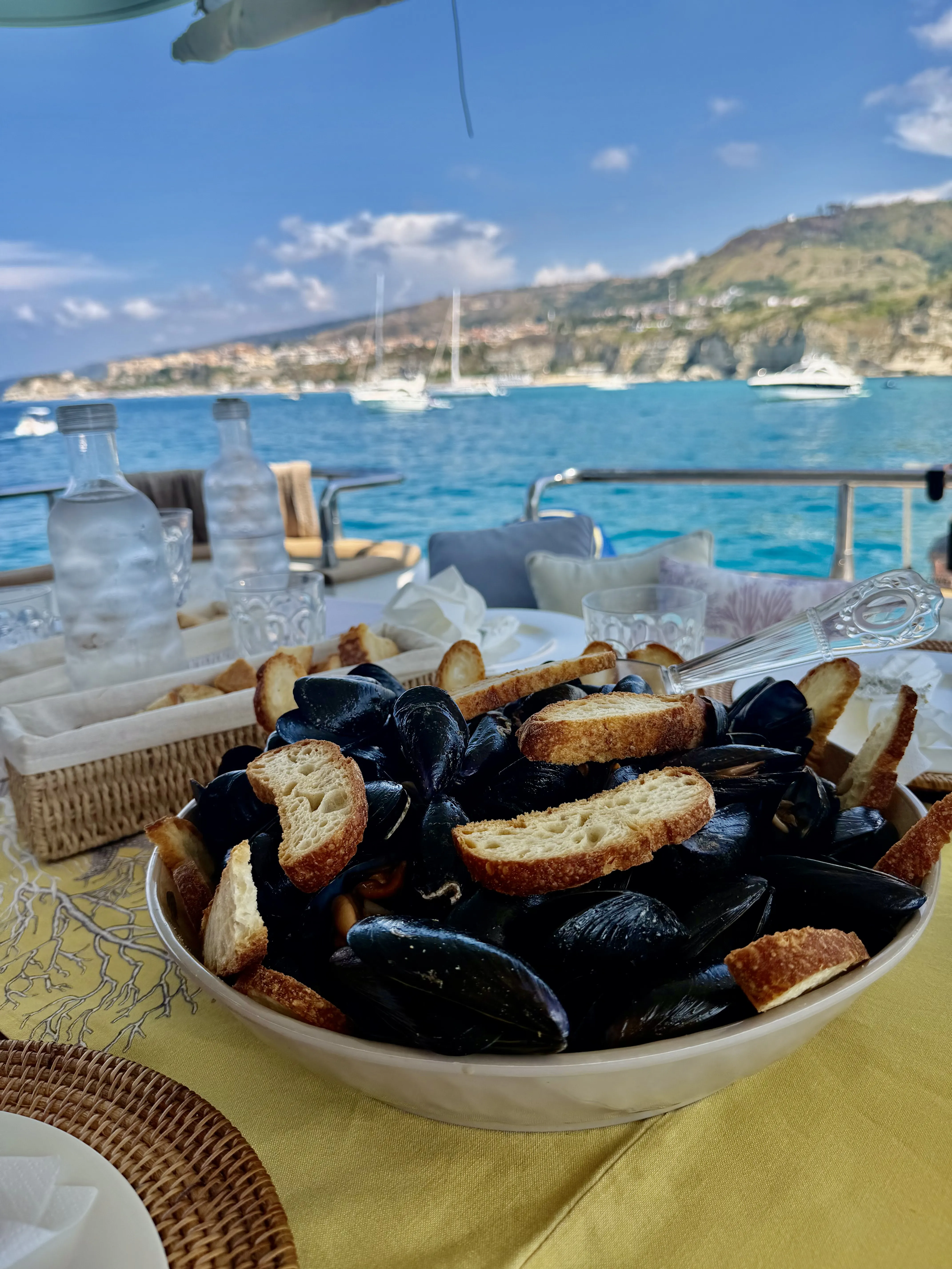 A bowl of mussels and crostini on the aft deck table, the bay and the coast beyond